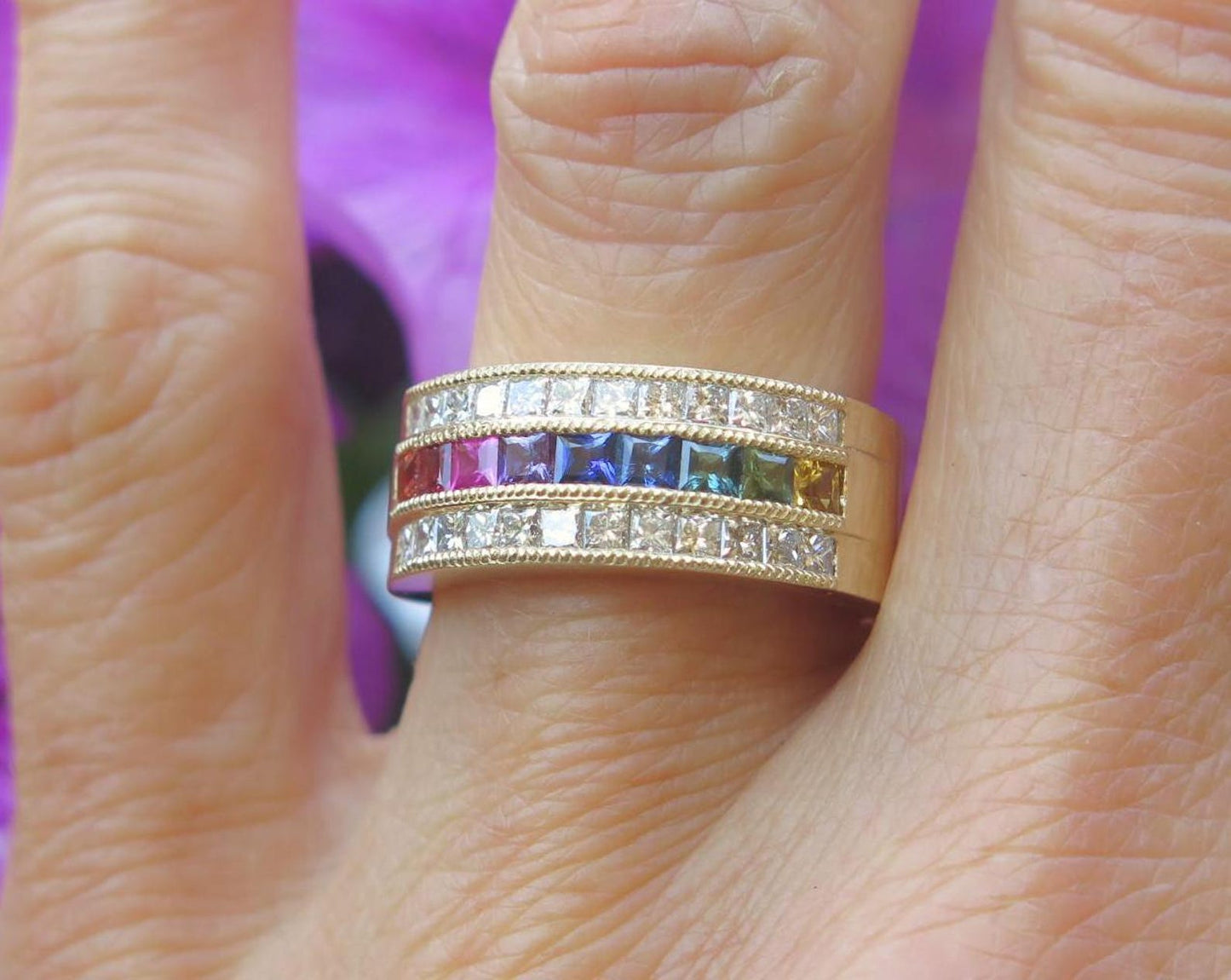close up of natural rainbow sapphire ring with princess cut gemstones on finger. Three fingers are showing.