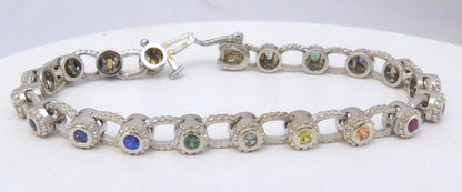 A white gold tennis bracelet with multiple round-cut rainbow sapphires in various colors including blue, green, yellow, orange, and pink, displayed on a white background.
