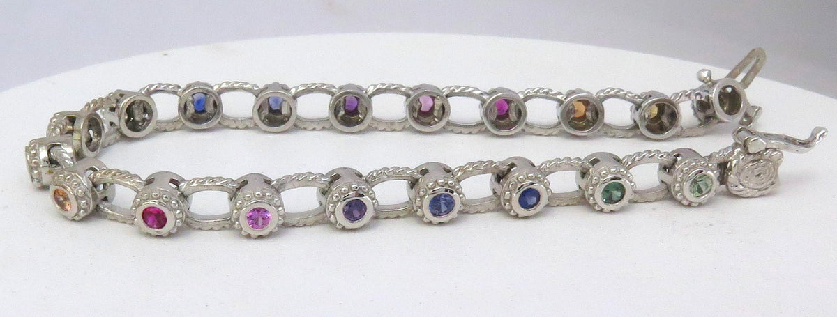 A 14k white gold textured bezel tennis bracelet with round-cut multicolor rainbow sapphire gemstones, displayed on a white background.