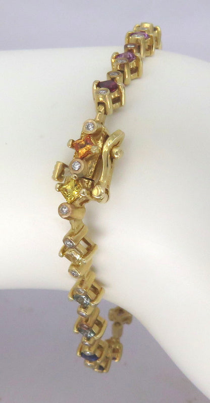 A yellow gold link bracelet displayed on a white mannequin arm. The bracelet features multiple links set with small gemstones, including purple, yellow, and clear stones, with a central decorative gold motif.