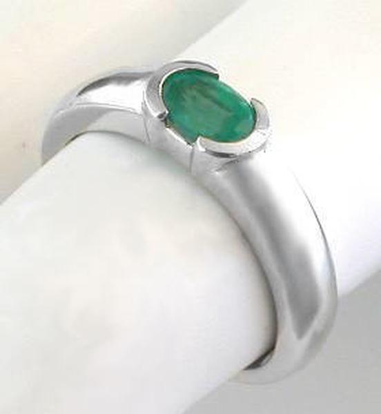 A white gold ring with an oval emerald, displayed on a white ring stand.