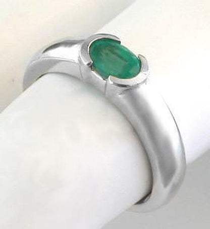 A white gold ring with an oval emerald, displayed on a white ring stand.