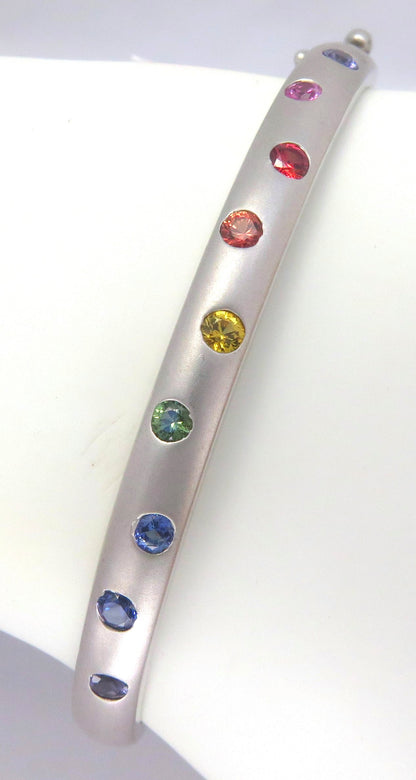 A burnished set rainbow sapphire bangle bracelet in white gold with a brushed finish, displayed on a white background.