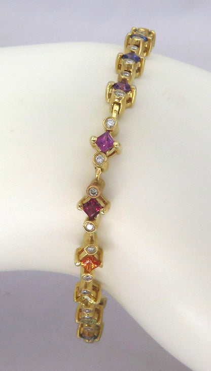 A gold tennis bracelet with alternating colored sapphire gemstone links, displayed on a white mannequin arm. The bracelet features purple, orange, and blue gemstones alongside clear diamonds.