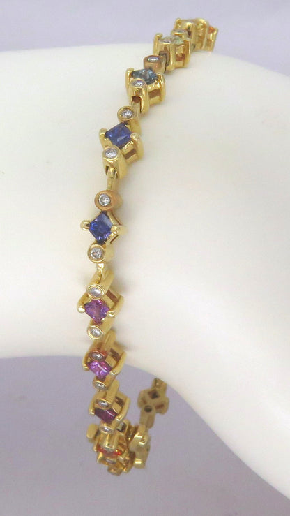 A gold-plated bracelet with alternating colored sapphire clusters, displayed on a white mannequin hand. The bracelet features blue, purple, and pink gemstones set in gold.