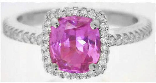 A silver-toned ring featuring a cushion-cut pink gemstone in a halo setting, with a pavé band adorned with small clear stones, shown against a plain white background.