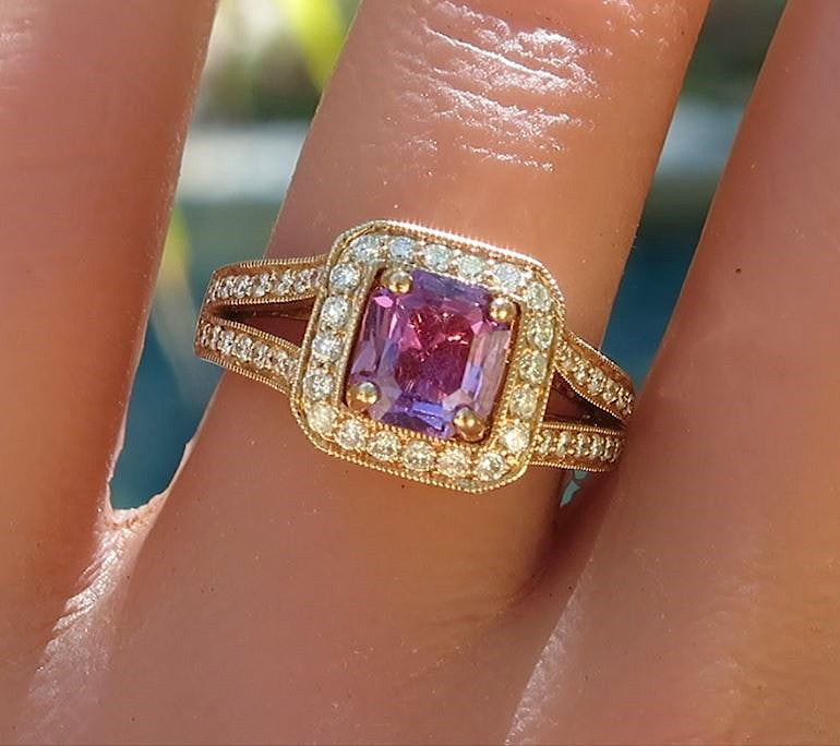A close-up of a rose gold ring with a square-cut magenta sapphire and small clear accent diamonds, worn on a finger.