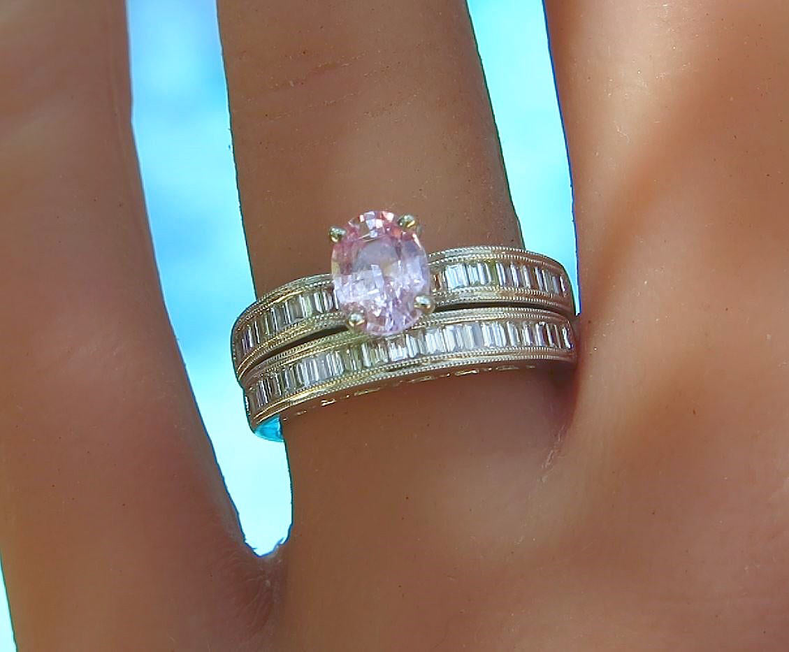 A close-up of a hand wearing a white gold engagement set with baguette diamonds and a central oval pink gemstone.