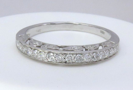 A white gold diamond band ring with a row of round-cut diamonds and an openwork pattern on the band, displayed on a white surface.