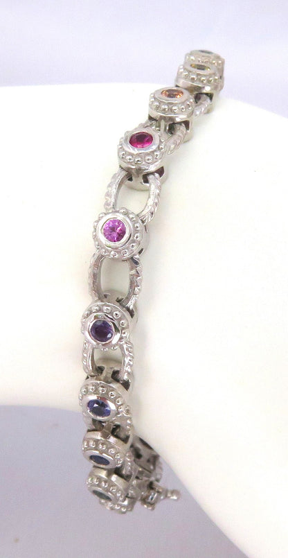 A white gold link bracelet displayed on a white mannequin arm, featuring alternating oval links with round pink, purple, and blue sapphires