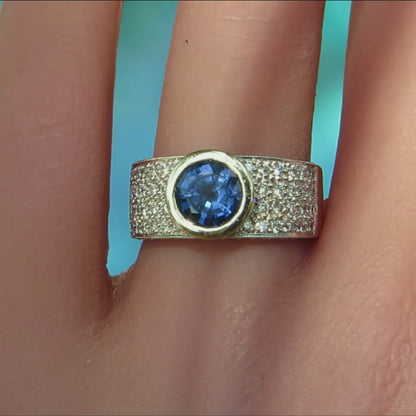 wide band ring with round bezel set blue sapphire and pave diamonds in white and yellow metal on ladies' hand
