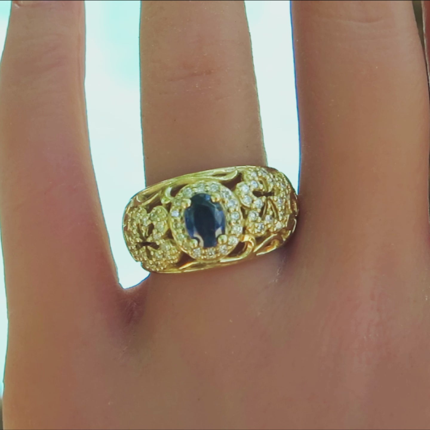 bold floral design ring with diamonds and center oval blue sapphire surrounded by diamond halo in yellow gold on the fing