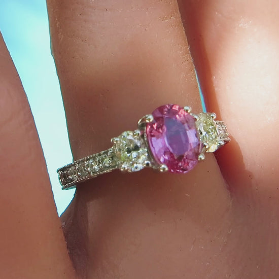 3 stone ring featuring three oval stones, pink sapphire, and 2 diamonds, in vintage inspired white gold ring on the finger