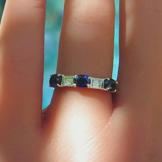three stone blue sapphire ring with two pairs of baguette diamonds in between in white gold metal on the finger