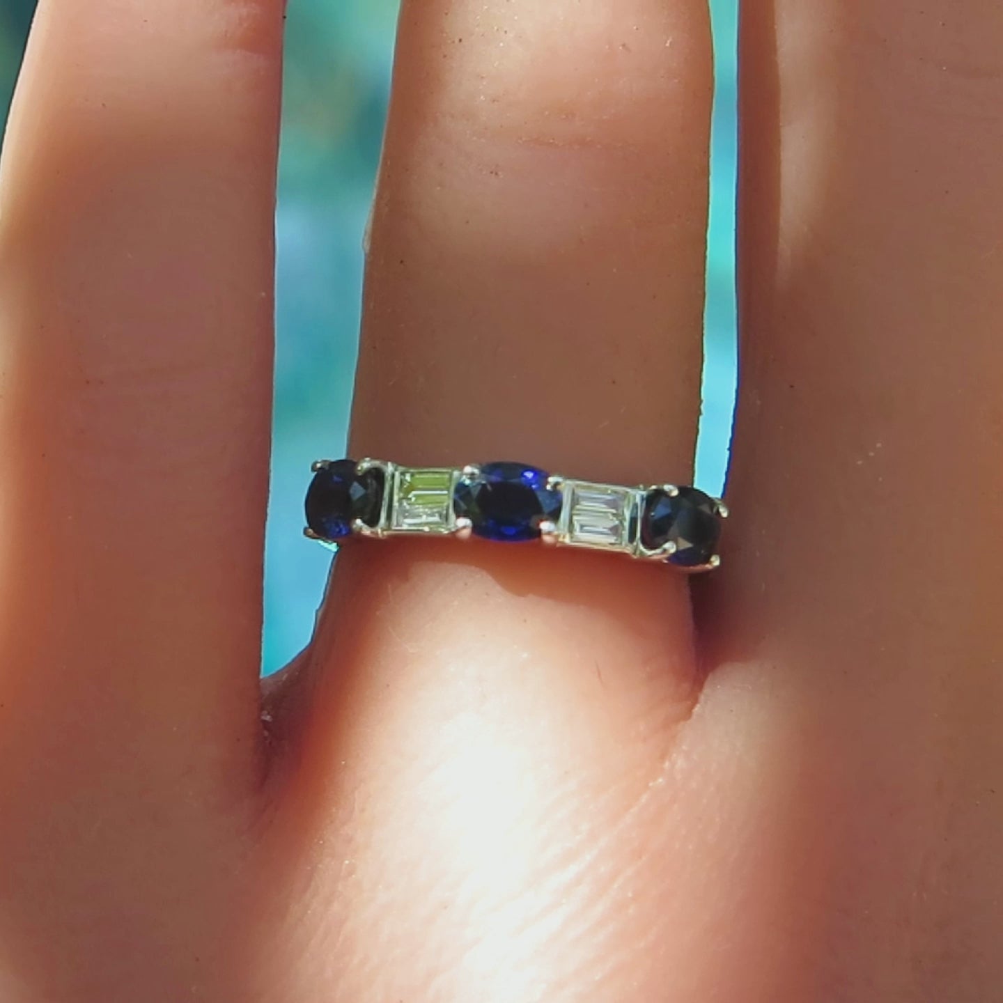 three stone blue sapphire ring with two pairs of baguette diamonds in between in white gold metal on the finger