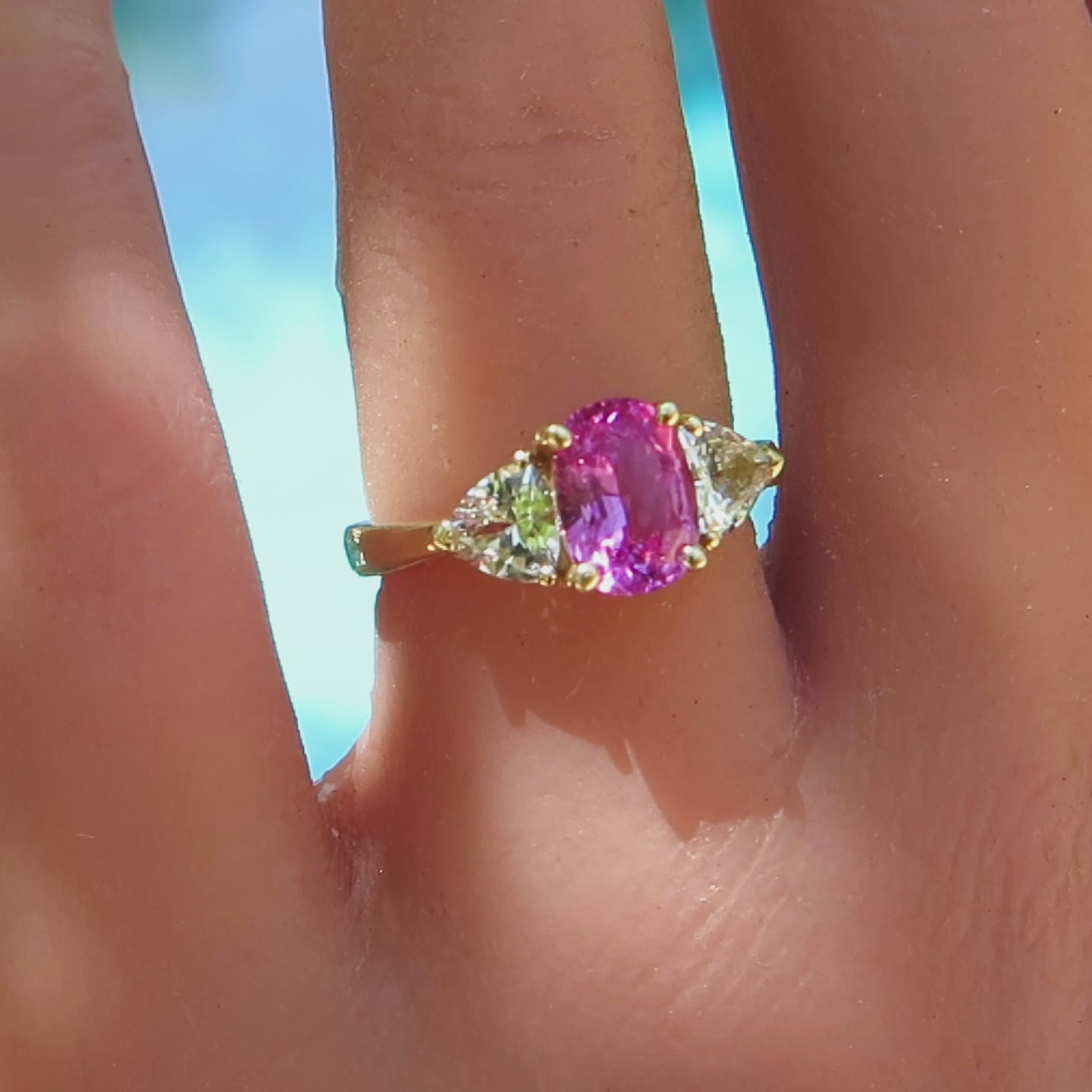 3 stone ring with bright pink oval sapphire and trillion cut side white sapphires in yellow gold on the finger