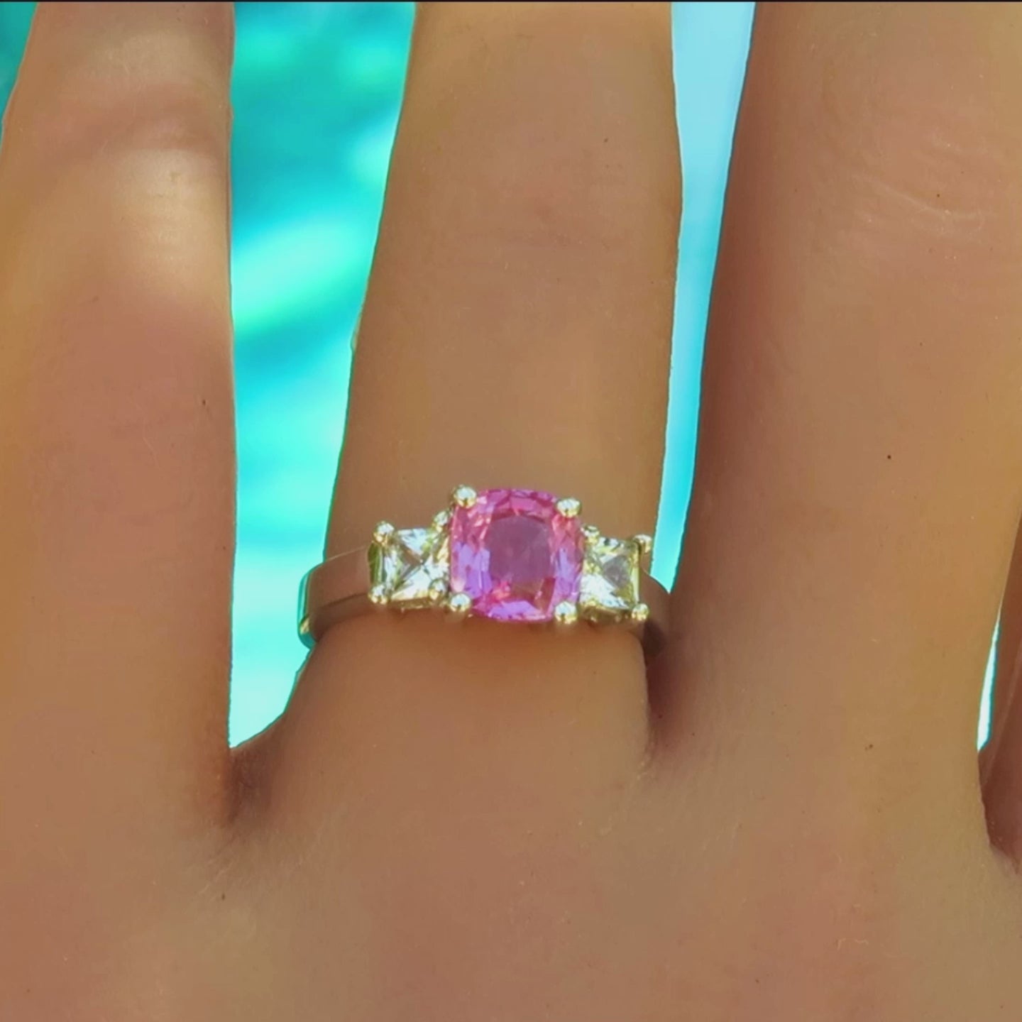 Three stone ring with a cushion cut pink sapphire and princess cut white sapphires in white metal platinum on the hand