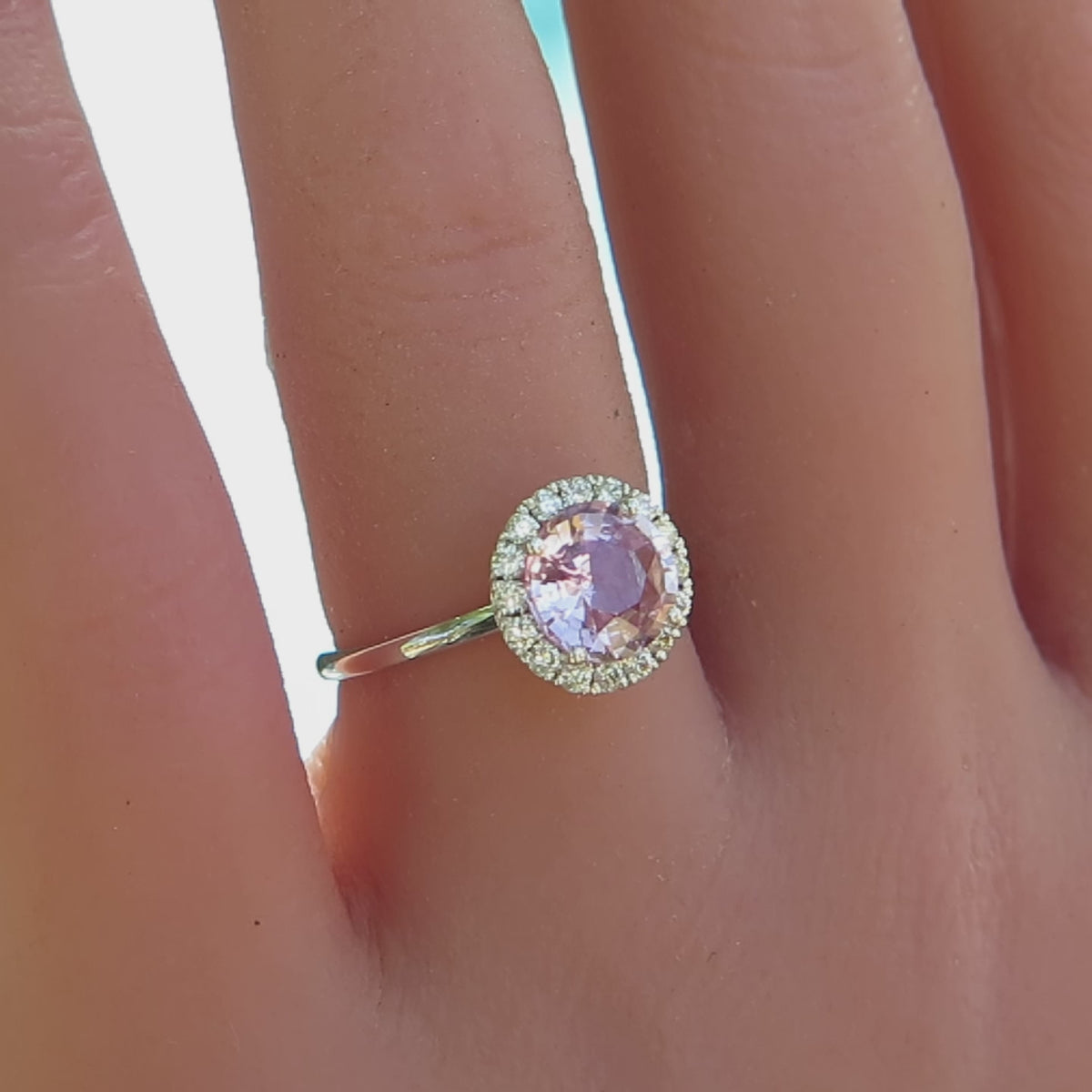 simple diamond halo ring with round light pink sapphire shown on the finger
