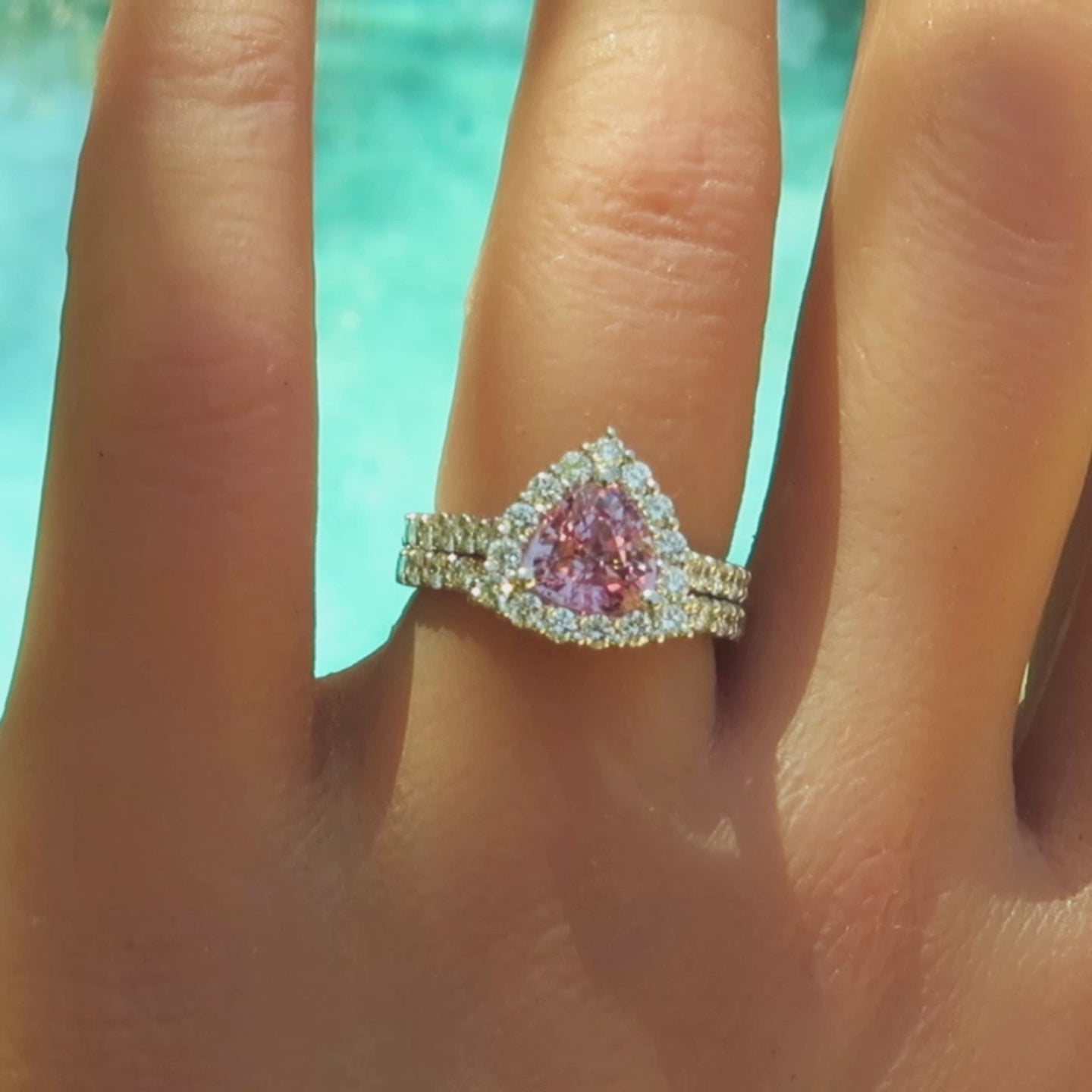 engagement ring and band with trillion cut light pink sapphire in a diamond halo setting in white metal platinum on the finger