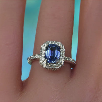 rectangular blue gemstone sapphire ring with clear stones surrounding center in white metal shown on the hand