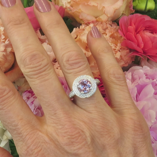 pastel floral background with cocktail style light pink sapphire and double diamond halo ring on the finger