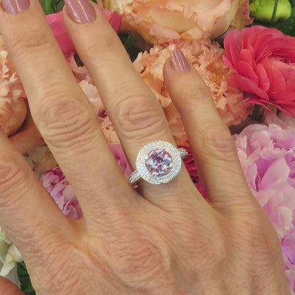 pastel floral background with cocktail style light pink sapphire and double diamond halo ring on the finger
