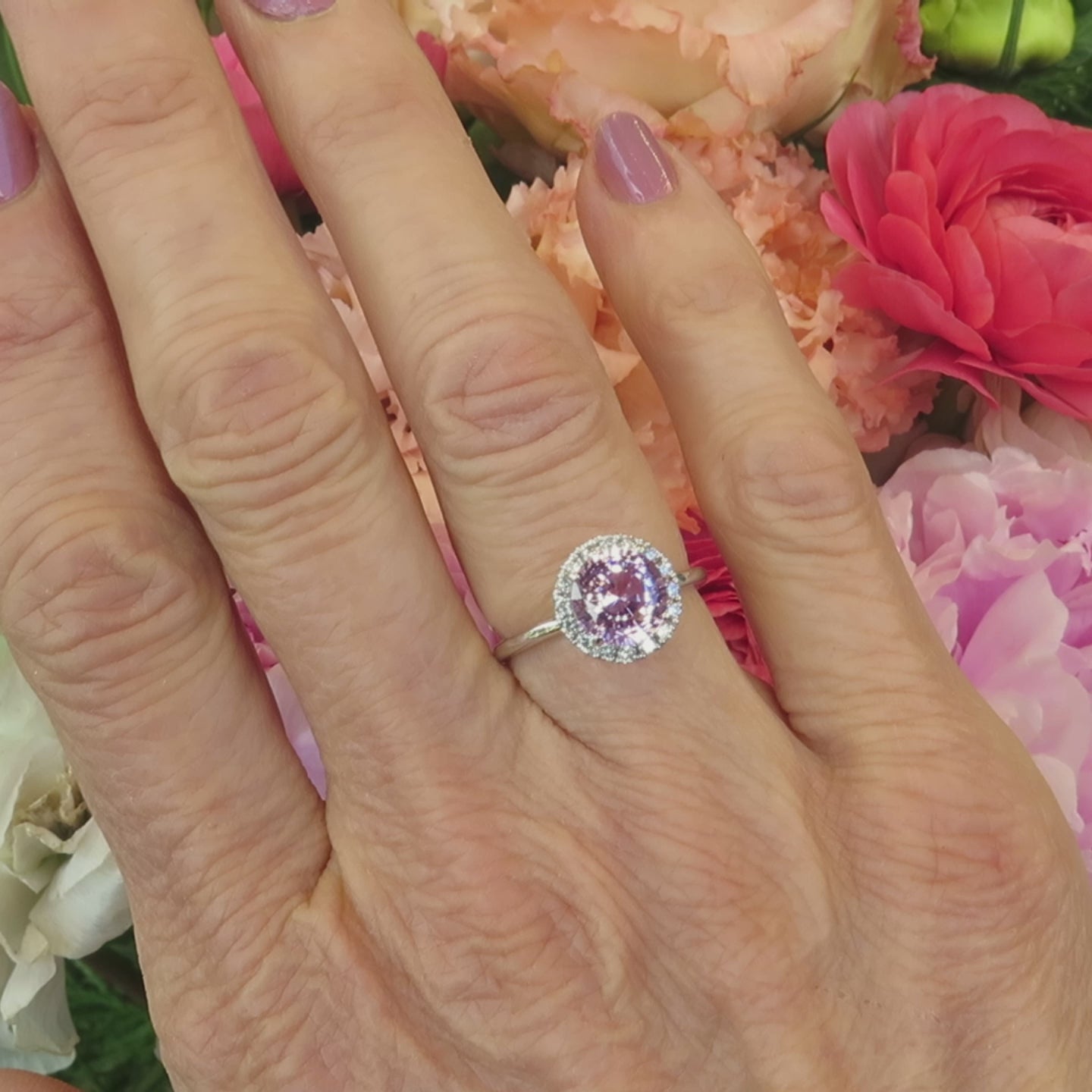 pale pink sapphire diamond halo ring with skinny band in white gold on the hand with a pastel floral background