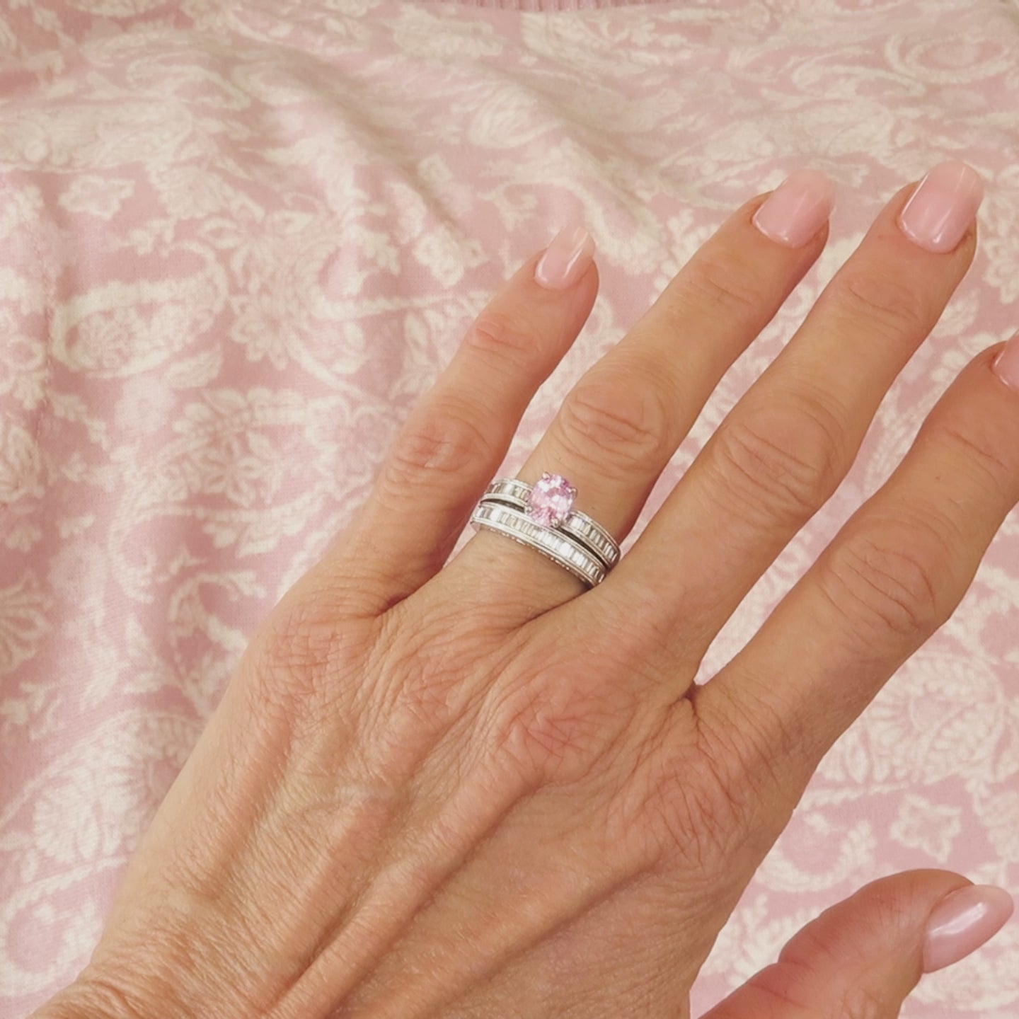 oval pink sapphire diamond wedding set in 18k white gold on the hand with a pink background