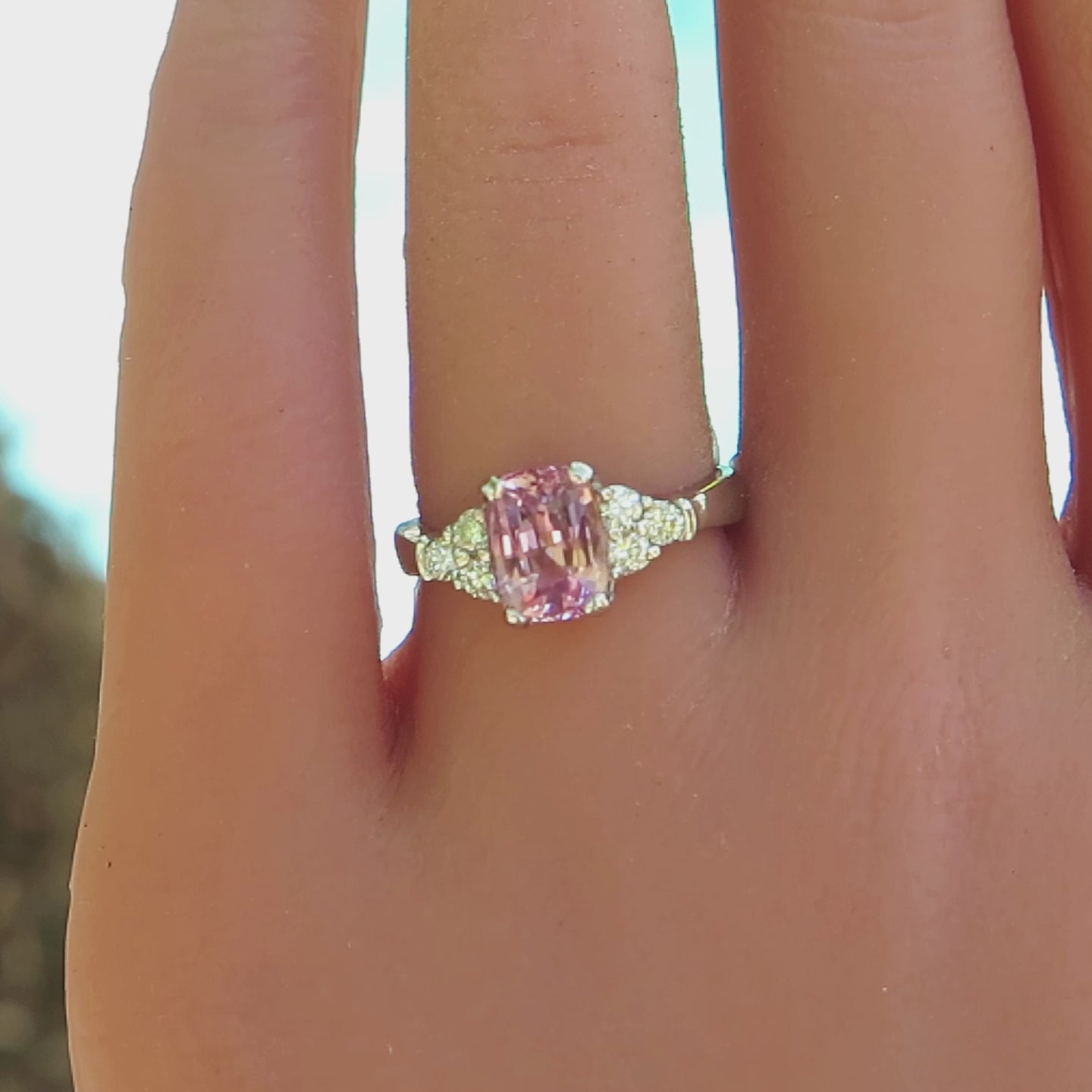 cushion cut light pink sapphire flanked by 3 round diamonds on each side in white gold on the hand