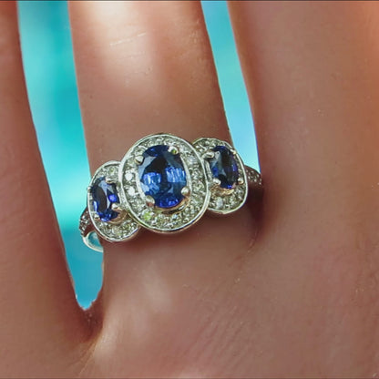 oval three stone ring with blue sapphires each surrounded by round diamonds on a ladies finger