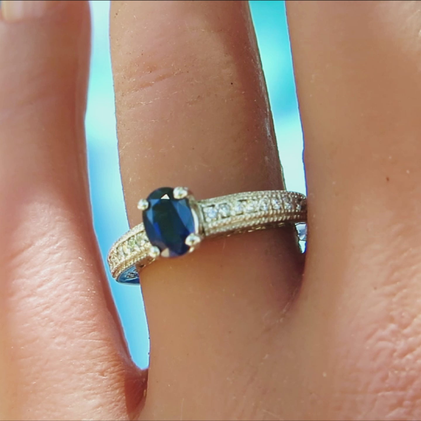 antique style blue sapphire and diamond ring with oval center stone and round side stones in white gold on the finger