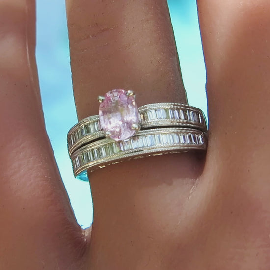 pastel pink oval sapphire with channel set baguette diamonds engagement ring and matching band in white metal on the hand