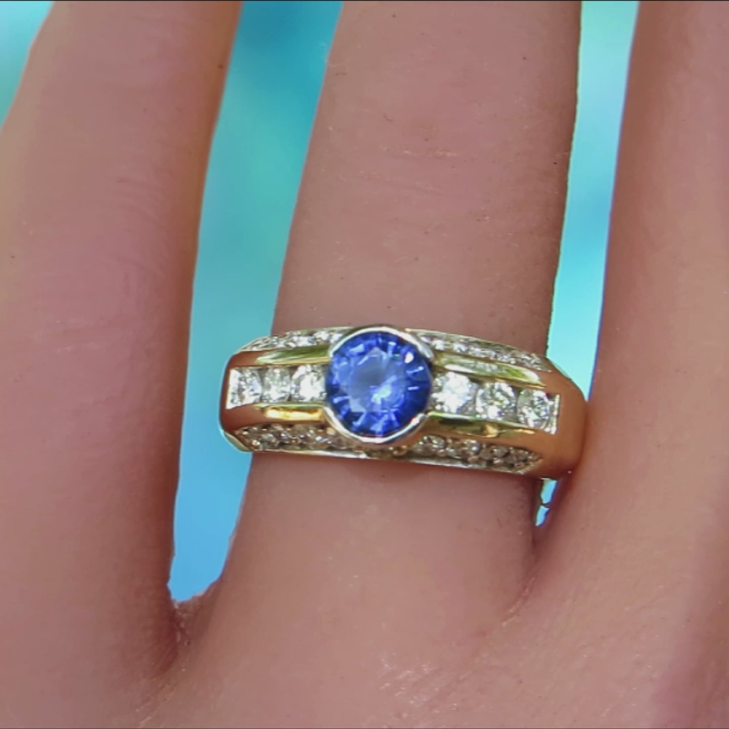 band style ring with three rows of channel and prong set round diamonds with semi bezel set round sapphire in yellow gold metal on the finger