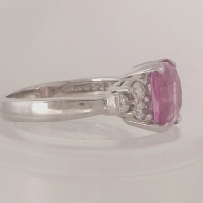 14k white gold ring with cushion cut pink sapphire at the center and 3 round diamonds on either side on a white turntable