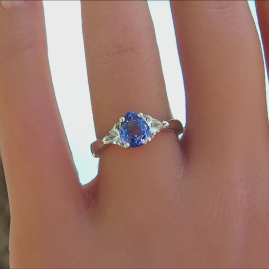three stone ring with pear cut blue sapphire and trillion white sapphire side stones in white gold on the finger