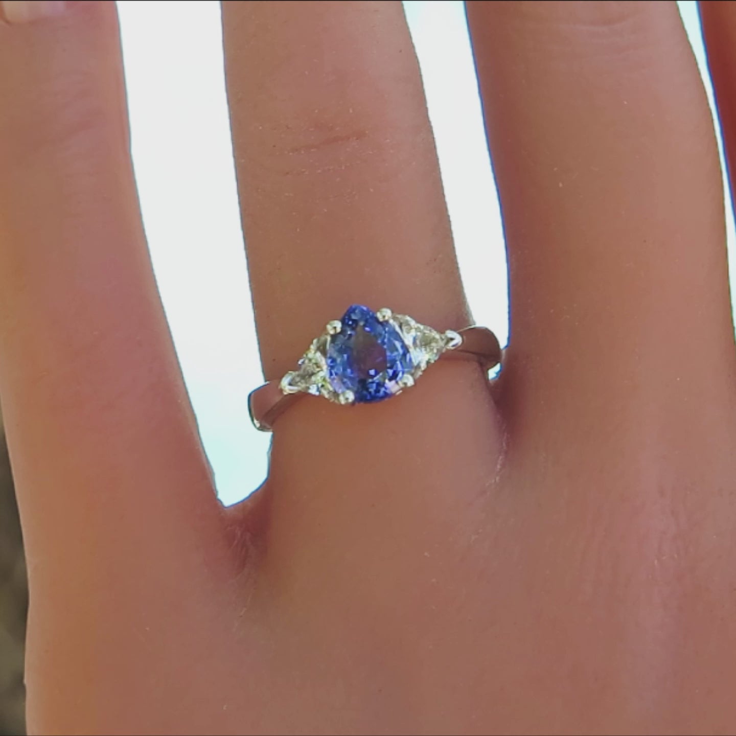 three stone ring with pear cut blue sapphire and trillion white sapphire side stones in white gold on the finger