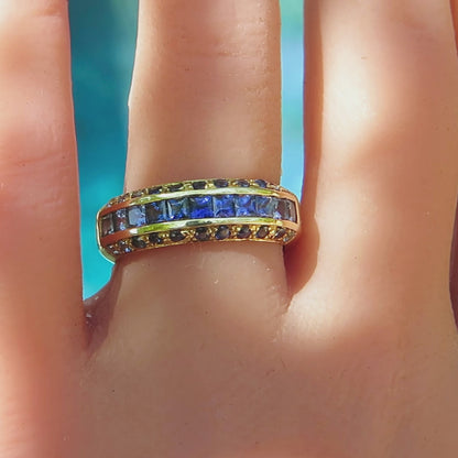 anniversary band with graduated shades of princess cut blue and round blue sapphires in yellow gold on the finger