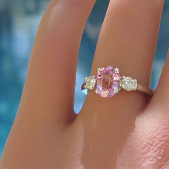 three stone oval pink sapphire and round diamond ring in white gold on the finger