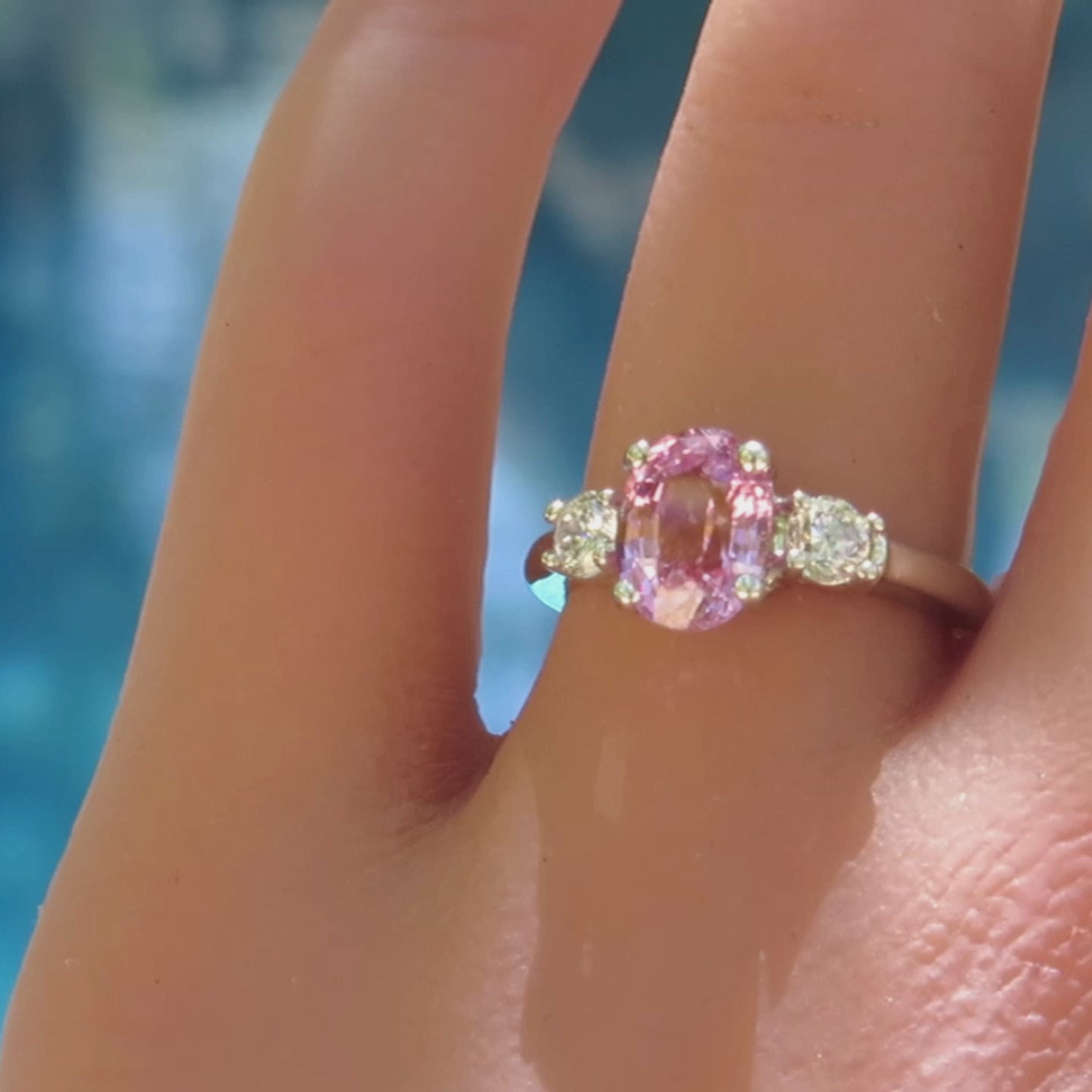 three stone oval pink sapphire and round diamond ring in white gold on the finger