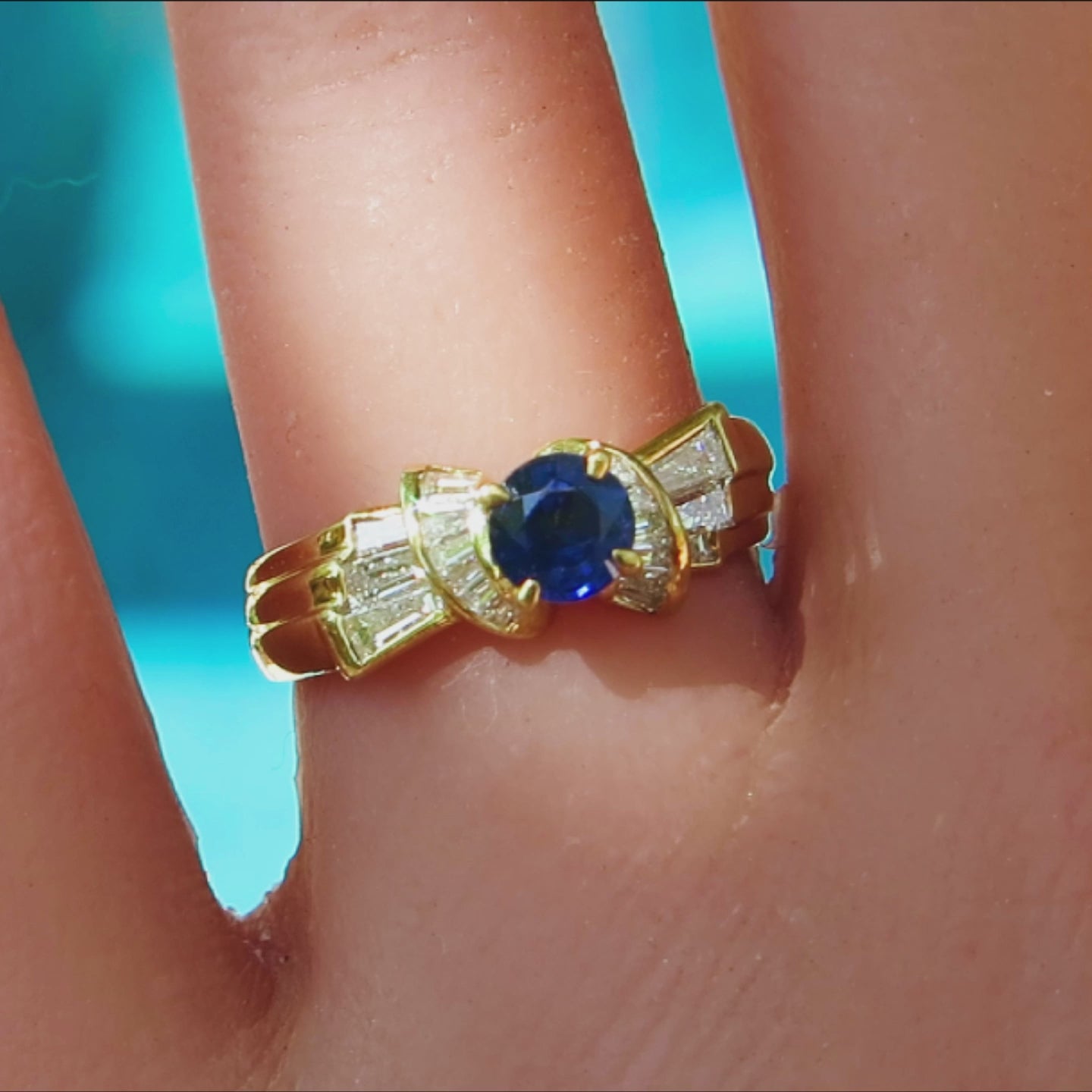 round blue sapphire with deep rich color flanked by flared baguette diamonds set in a rich yellow gold setting on the finger