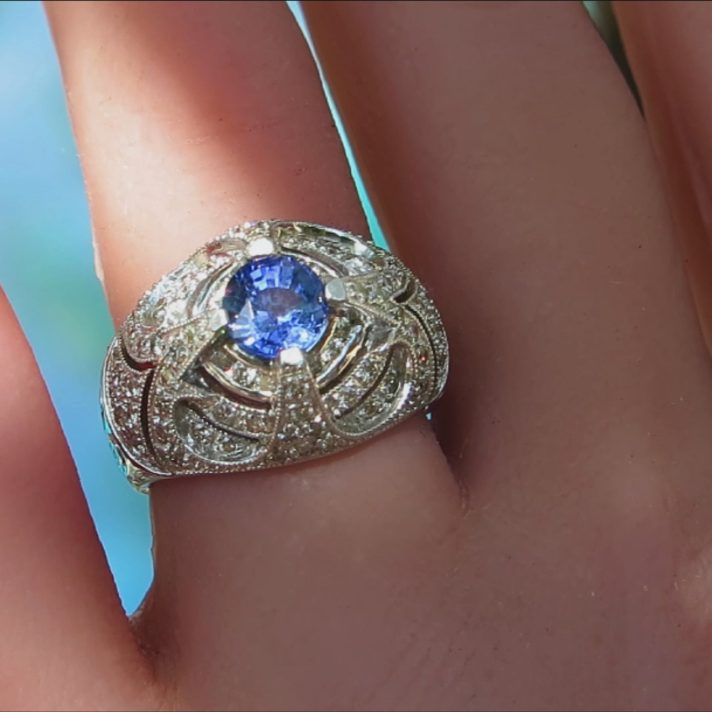 bold vintage style ring with round blue sapphire at the center and concentric circles of clear diamonds in a dome style ring in 14k white gold on the finger