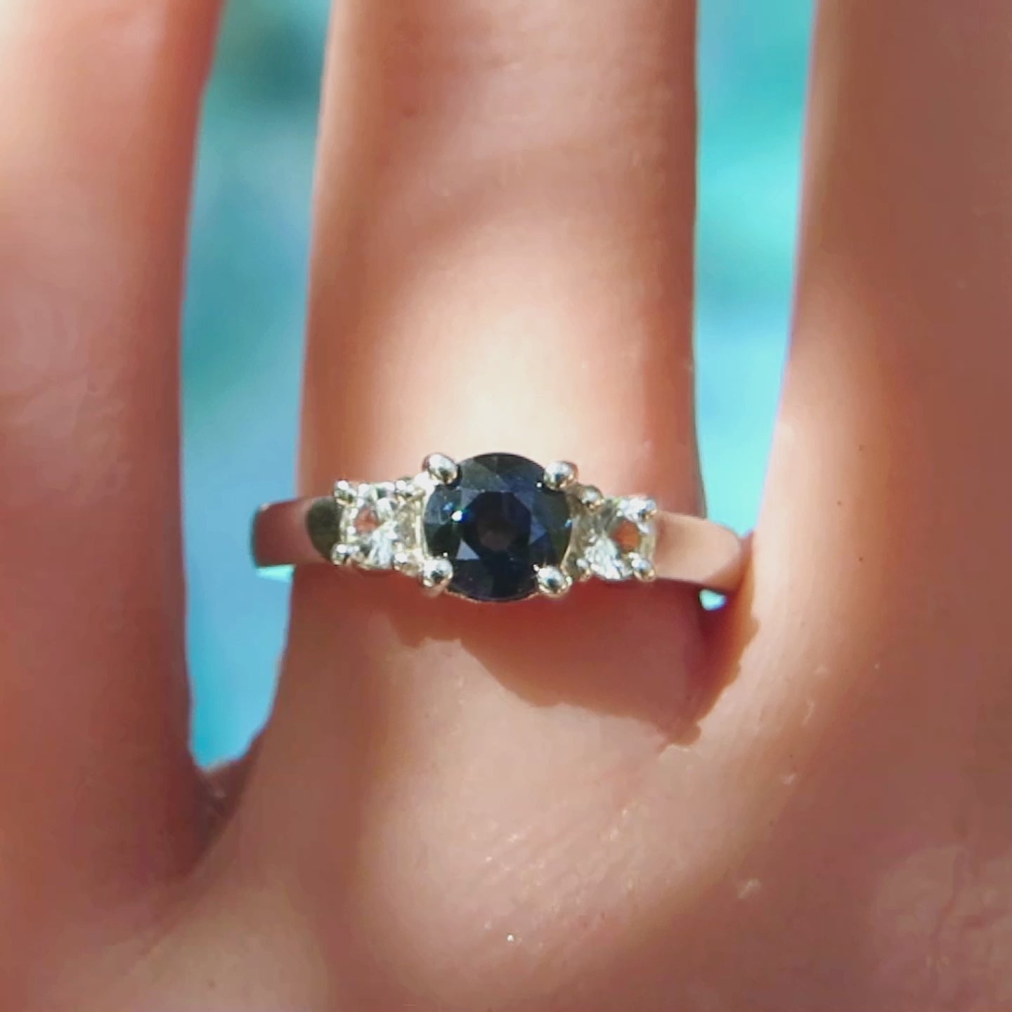 three stone dark blue sapphire and white sapphire ring on the finger