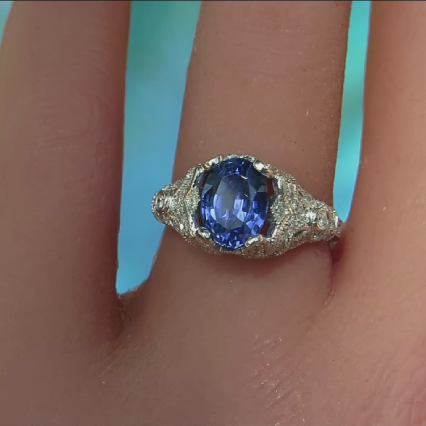 ornate vintage style oval sapphire ring in white platinum metal on ladies finger with blue background
