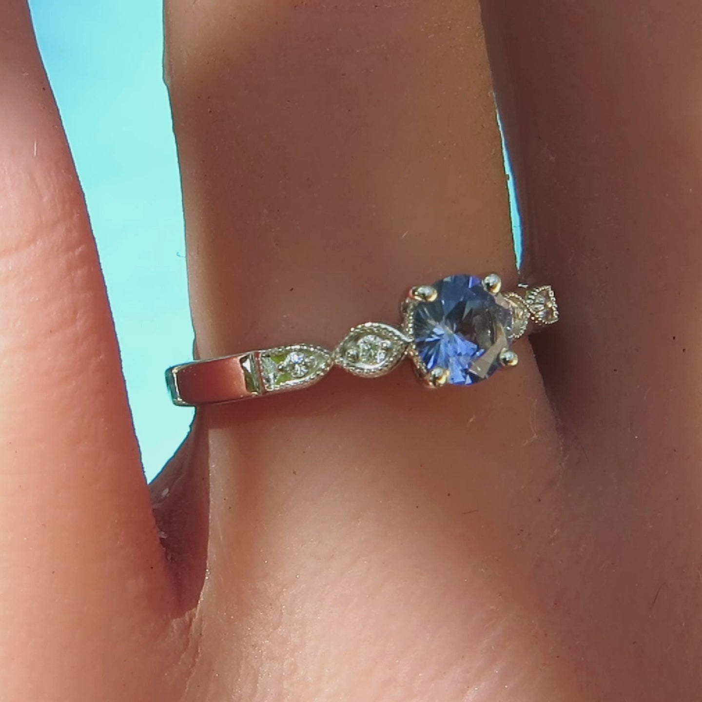 delicate sapphire and diamond ring with round sapphire and milgrain edging shown on the hand