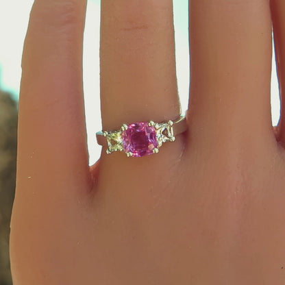 3 stone ring with bright pink sapphire and princess cut side white sapphires in white metal on the hand