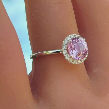 pastel pink round sapphire surrounded by a halo of diamonds with a skinny band of white gold on the finger