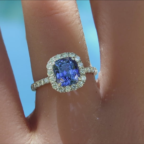 cushion cut blue sapphire diamond halo ring in white gold metal shown on the hand