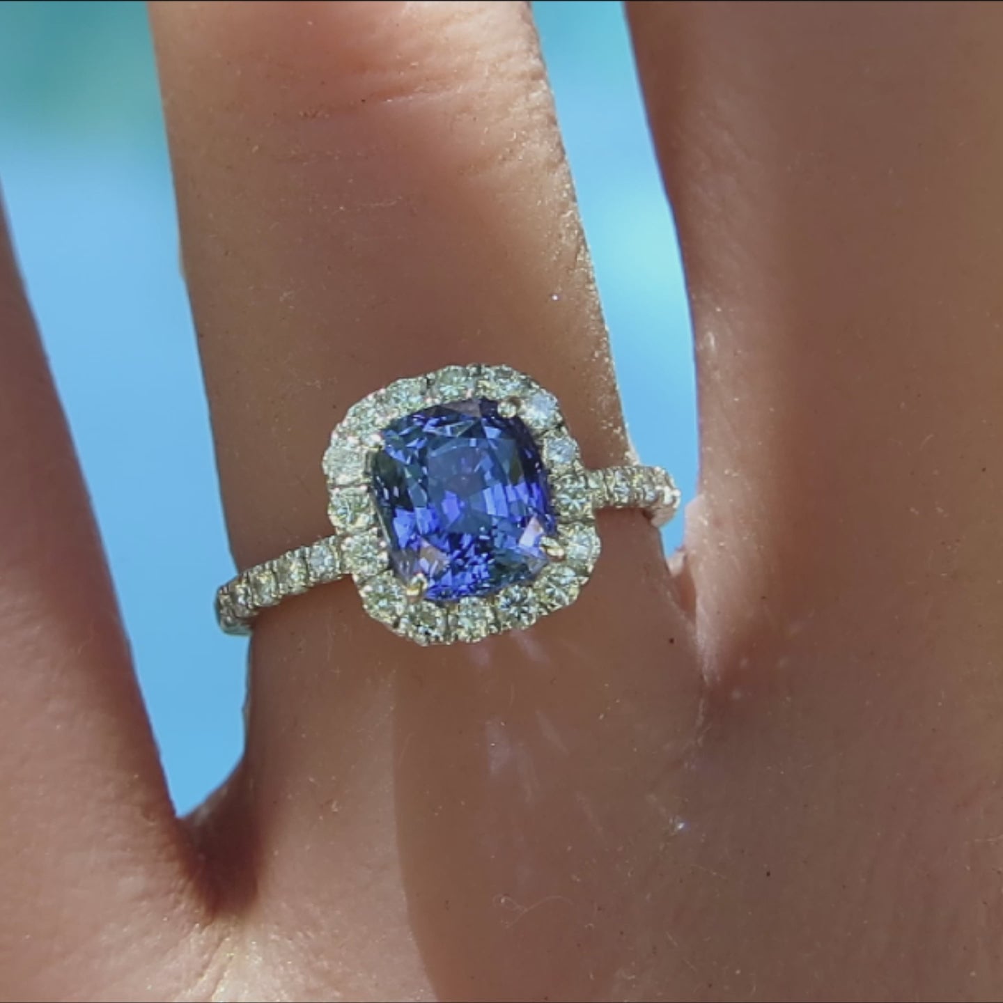 cushion cut blue sapphire diamond halo ring in white gold metal shown on the hand