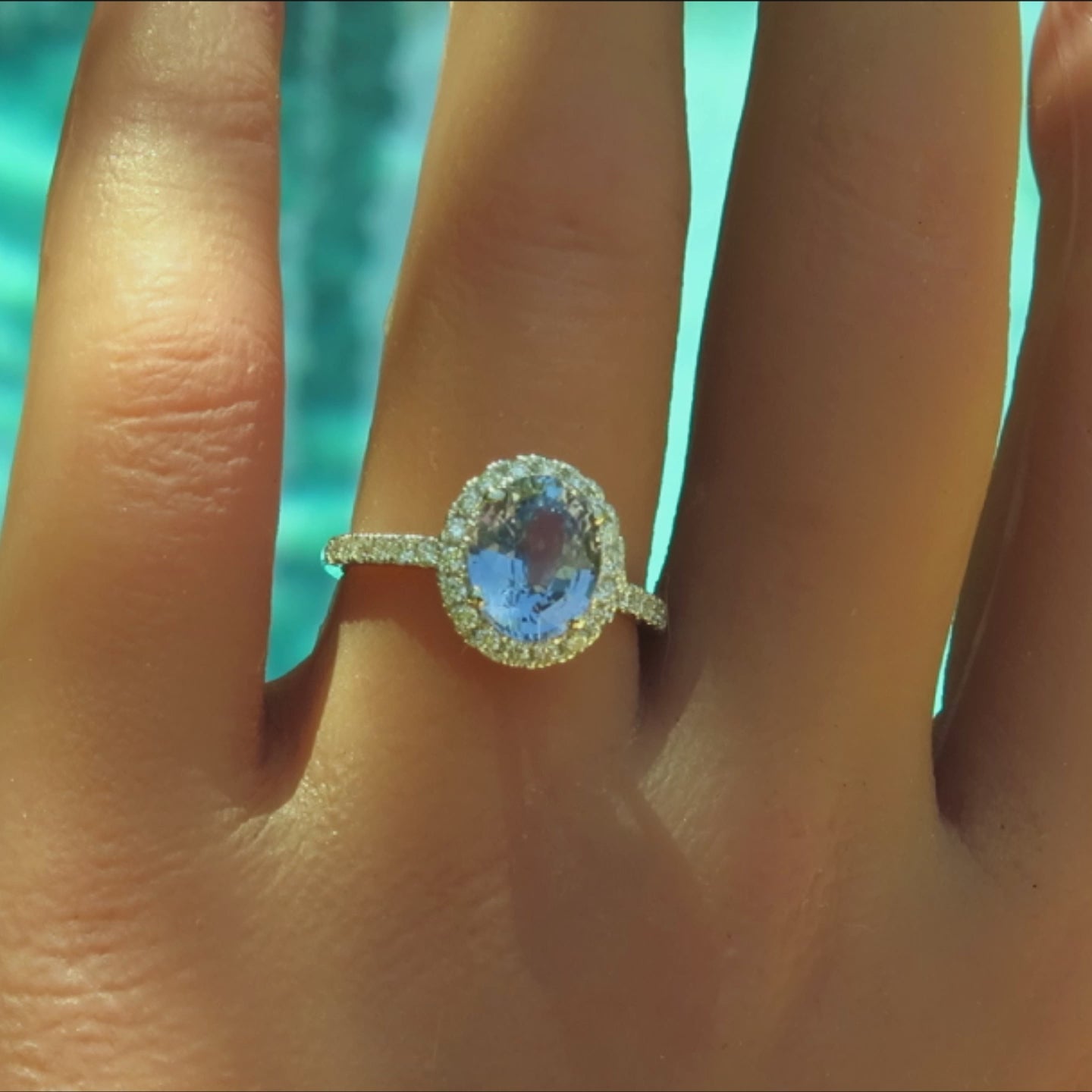 light blue oval sapphire surrounded by round diamonds with a skinny band of diamonds on a hand
