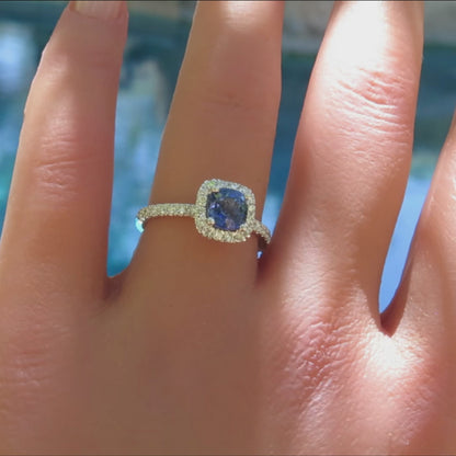 Cushion cut blue sapphire surrounded by diamonds with a simple band on the finger